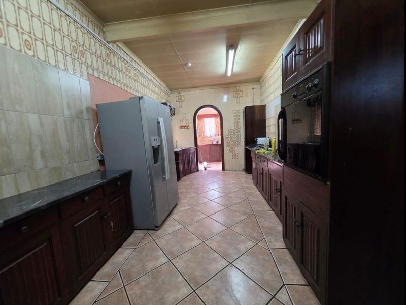 A dated kitchen featuring dark wood cabinetry, tiled walls, and tiled flooring, offering a functional layout with built-in oven and ample storage space.