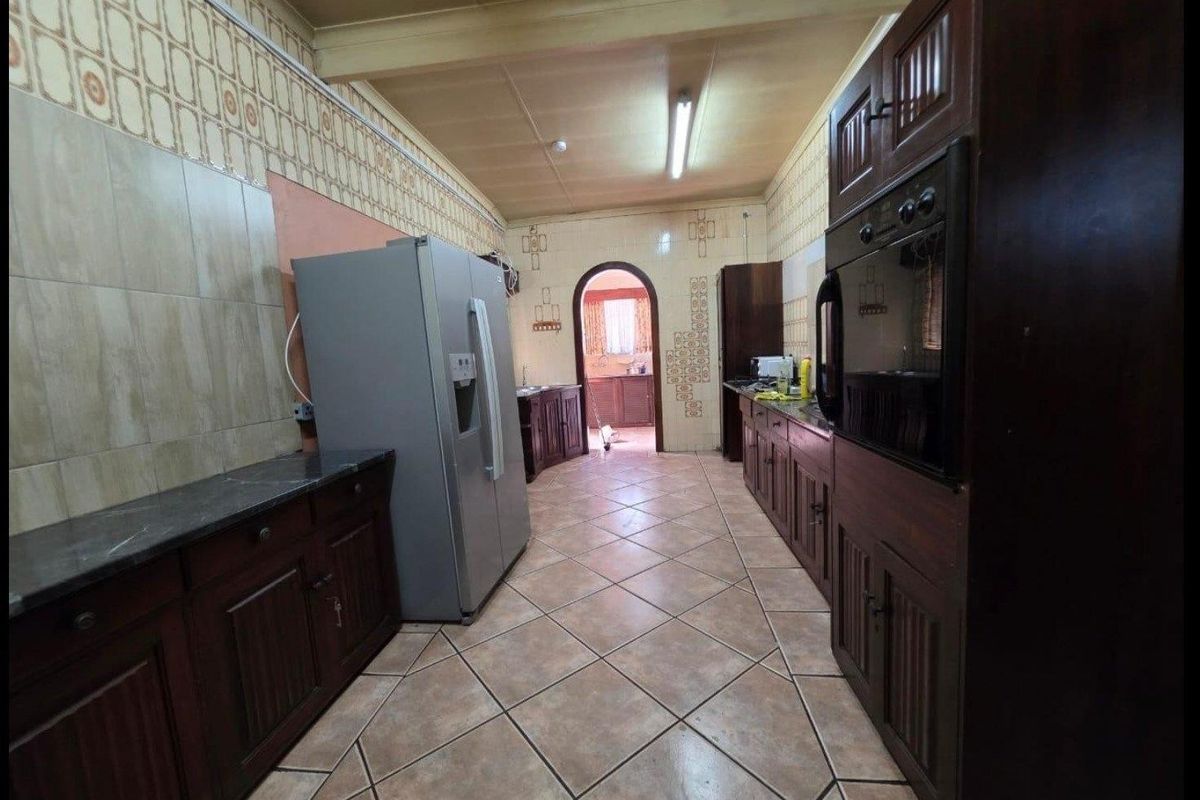 A dated kitchen featuring dark wood cabinetry, tiled walls, and tiled flooring, offering a functional layout with built-in oven and ample storage space.