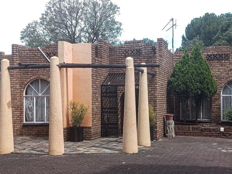 Front elevation of a face brick house featuring arched windows, a covered pergola entrance with concrete pillars, and a paved driveway.