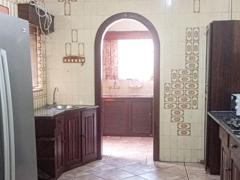 A dated kitchen featuring traditional cabinetry, stone countertops, and a gas hob, with an arched doorway leading to an adjacent scullery or utility area.
