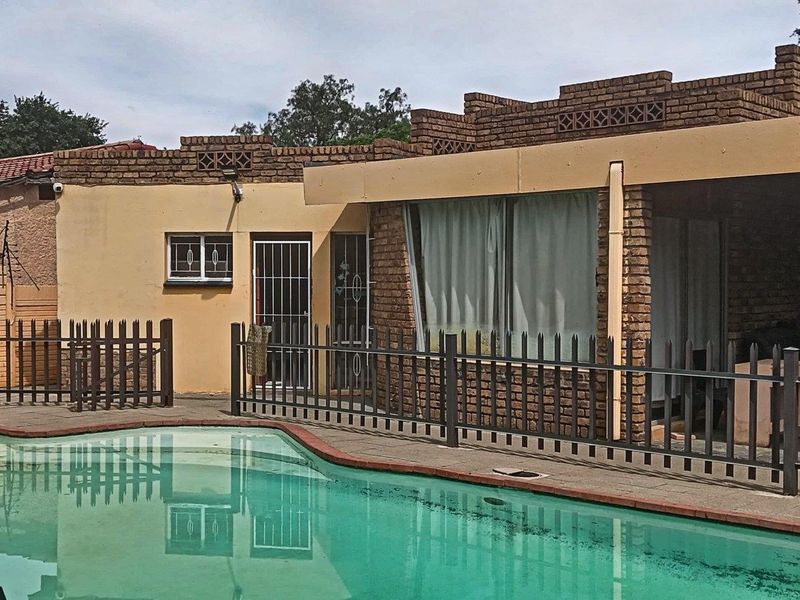 Rear exterior view featuring a swimming pool, security fencing, and a covered patio area attached to the main brick residence.