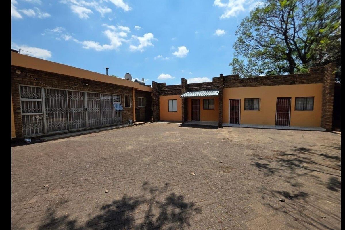 A spacious paved rear courtyard area featuring brick exterior walls and multiple access points with security gates.