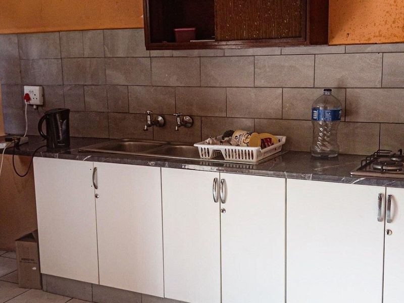 A functional kitchen featuring white cabinetry, a laminate countertop, a stainless steel double sink, and a built-in gas hob with a tiled backsplash.