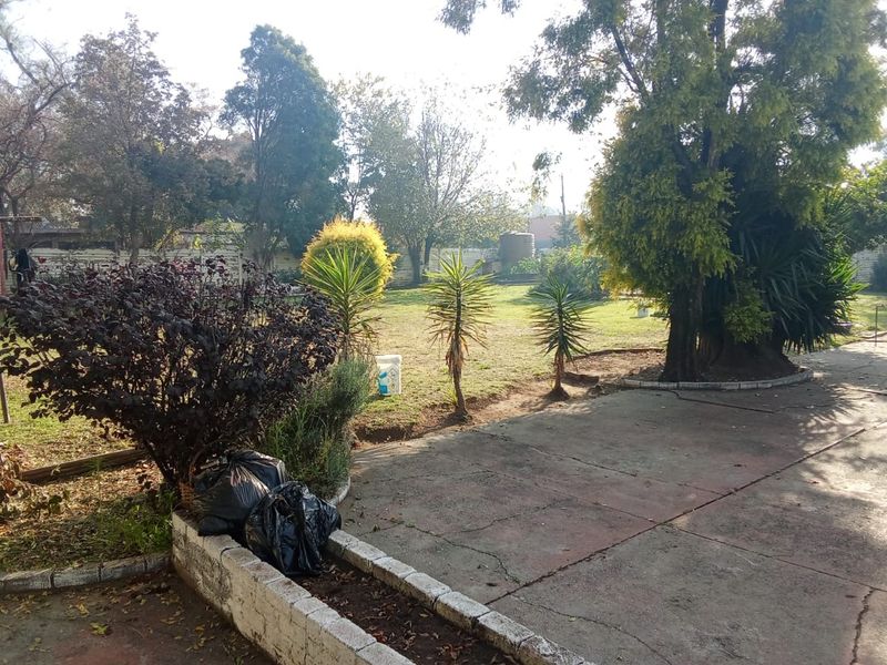 Spacious garden area featuring mature trees, established landscaping, a concrete patio, and a raised brick planter box.