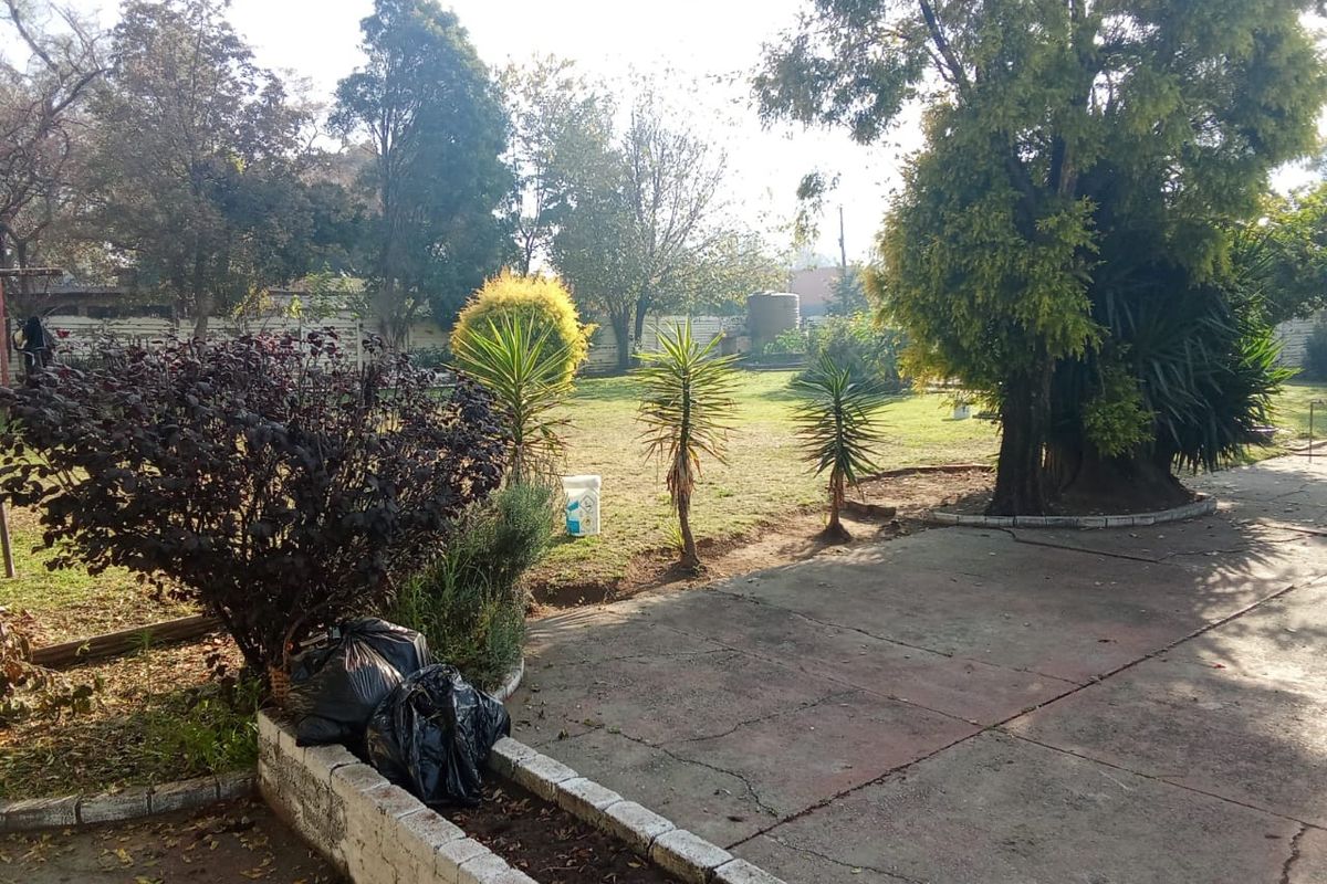 Spacious garden area featuring mature trees, established landscaping, a concrete patio, and a raised brick planter box.