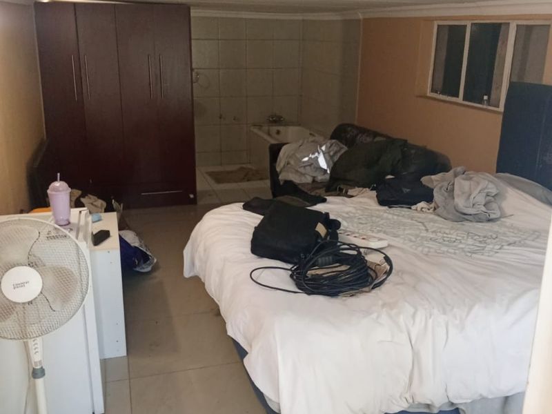 A bedroom featuring tiled flooring, a built-in wardrobe, and an open-plan en-suite bathtub area with visible ceiling and wall wear.