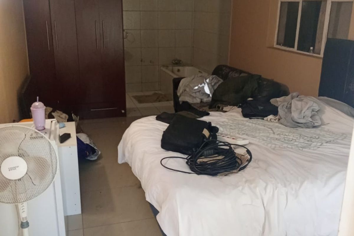 A bedroom featuring tiled flooring, a built-in wardrobe, and an open-plan en-suite bathtub area with visible ceiling and wall wear.