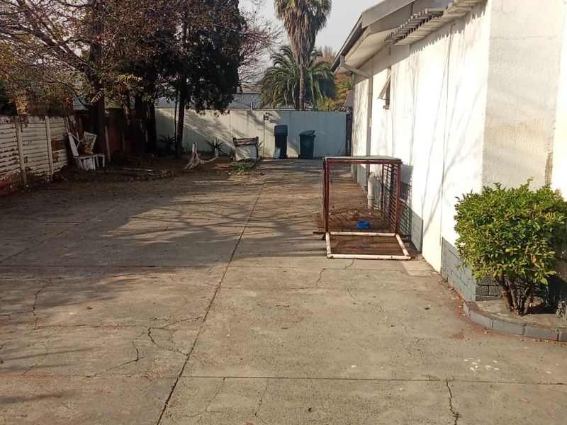 A rear exterior view showing a large concrete driveway area with boundary walls and mature trees.
