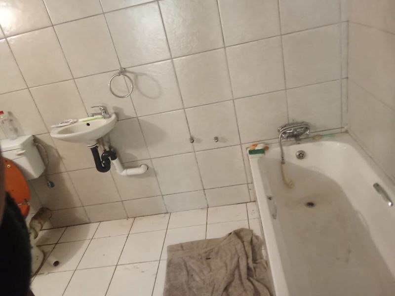 A dated bathroom featuring a wall-mounted basin, bathtub, and full-height ceramic tiling, requiring cosmetic updates and maintenance to improve its overall condition.