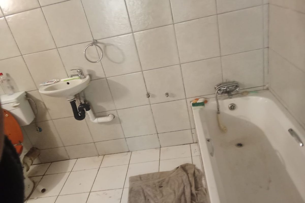 A dated bathroom featuring a wall-mounted basin, bathtub, and full-height ceramic tiling, requiring cosmetic updates and maintenance to improve its overall condition.