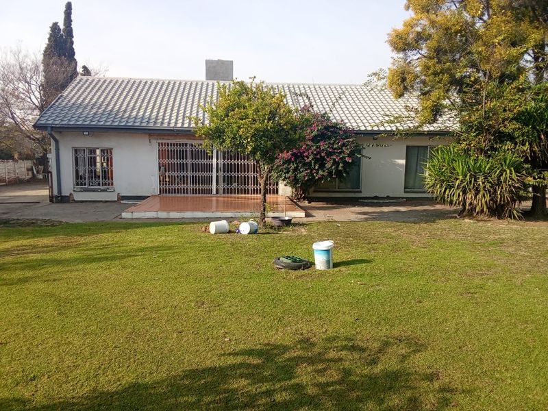 Rear view of the house featuring a tiled roof, a small tiled patio area, and a spacious garden with a concrete driveway.