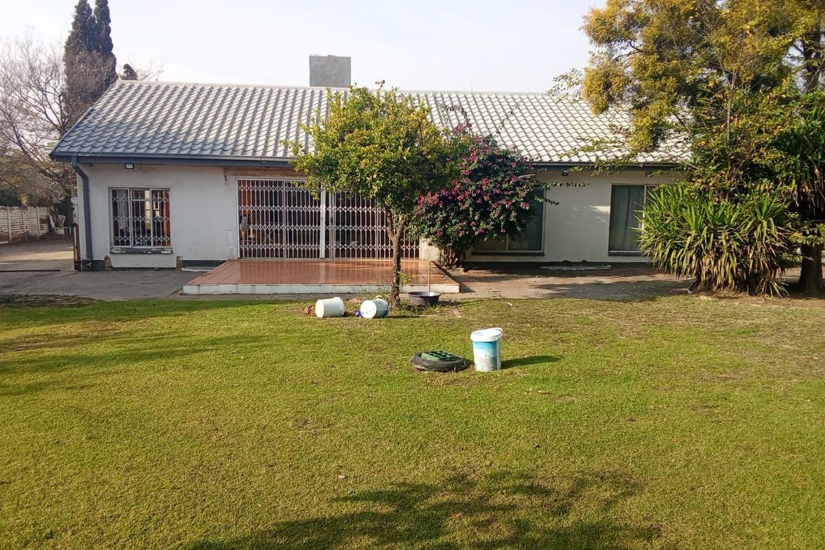 Rear view of the house featuring a tiled roof, a small tiled patio area, and a spacious garden with a concrete driveway.