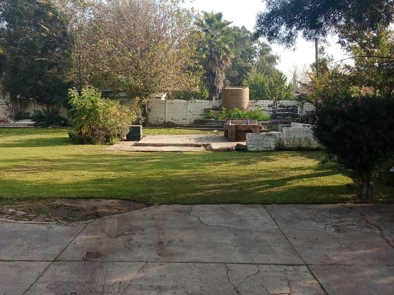 Spacious backyard featuring a large lawn, concrete patio area, built-in braai, and a water tank, enclosed by a boundary wall.