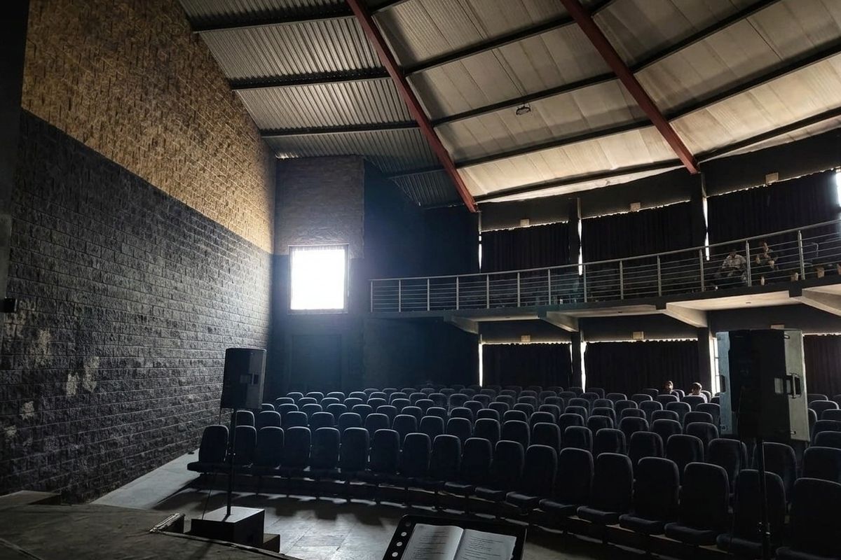 Spacious auditorium or cinema room featuring tiered seating, a mezzanine level, and industrial-style exposed steel roof trusses with high ceilings.