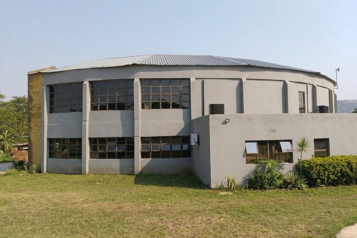 A view of the rear exterior of a commercial building featuring a circular design, metal roofing, and multiple aluminium-framed windows.