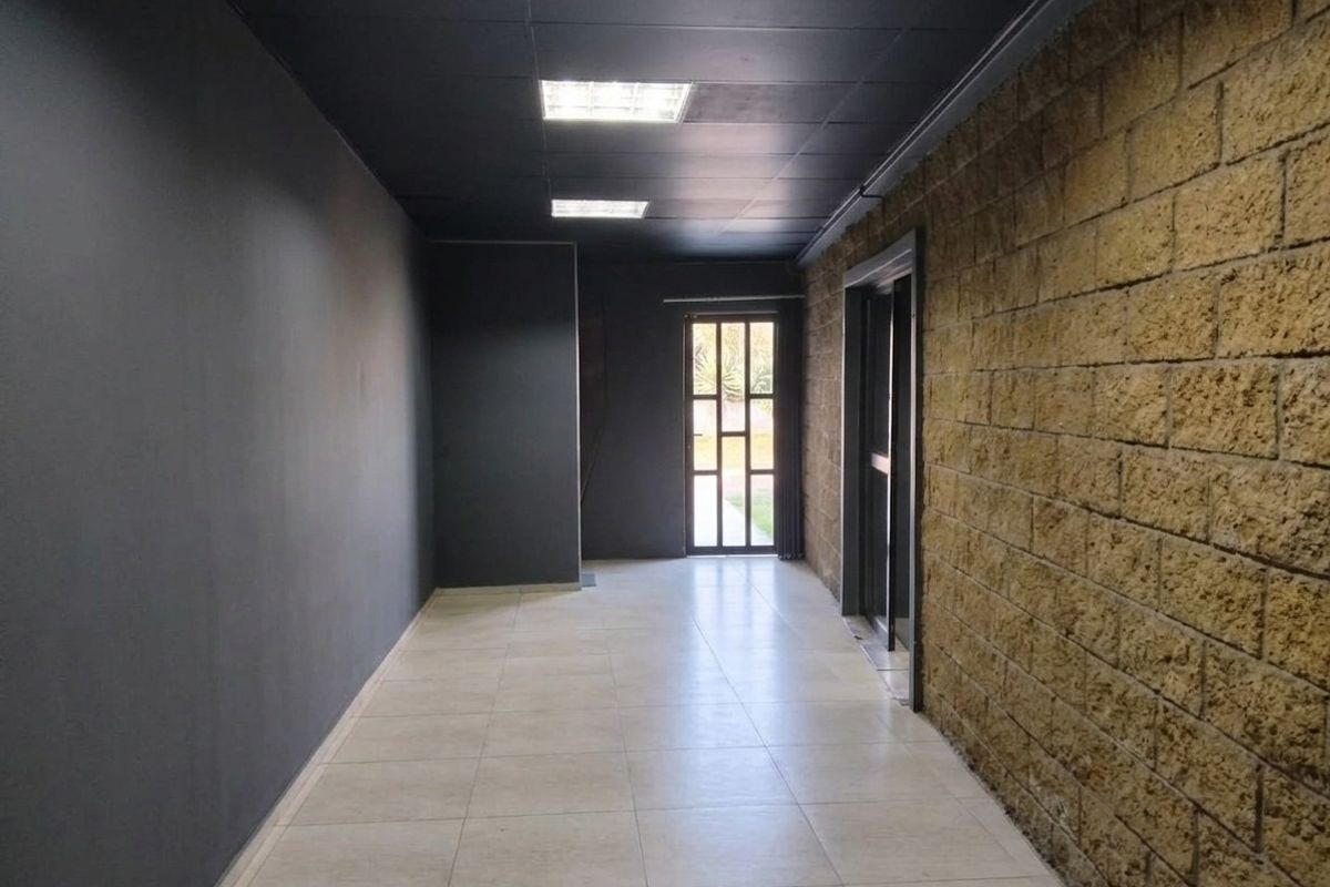 A modern commercial hallway featuring a striking contrast between a dark painted wall, exposed brickwork, tiled flooring, and recessed ceiling lighting.
