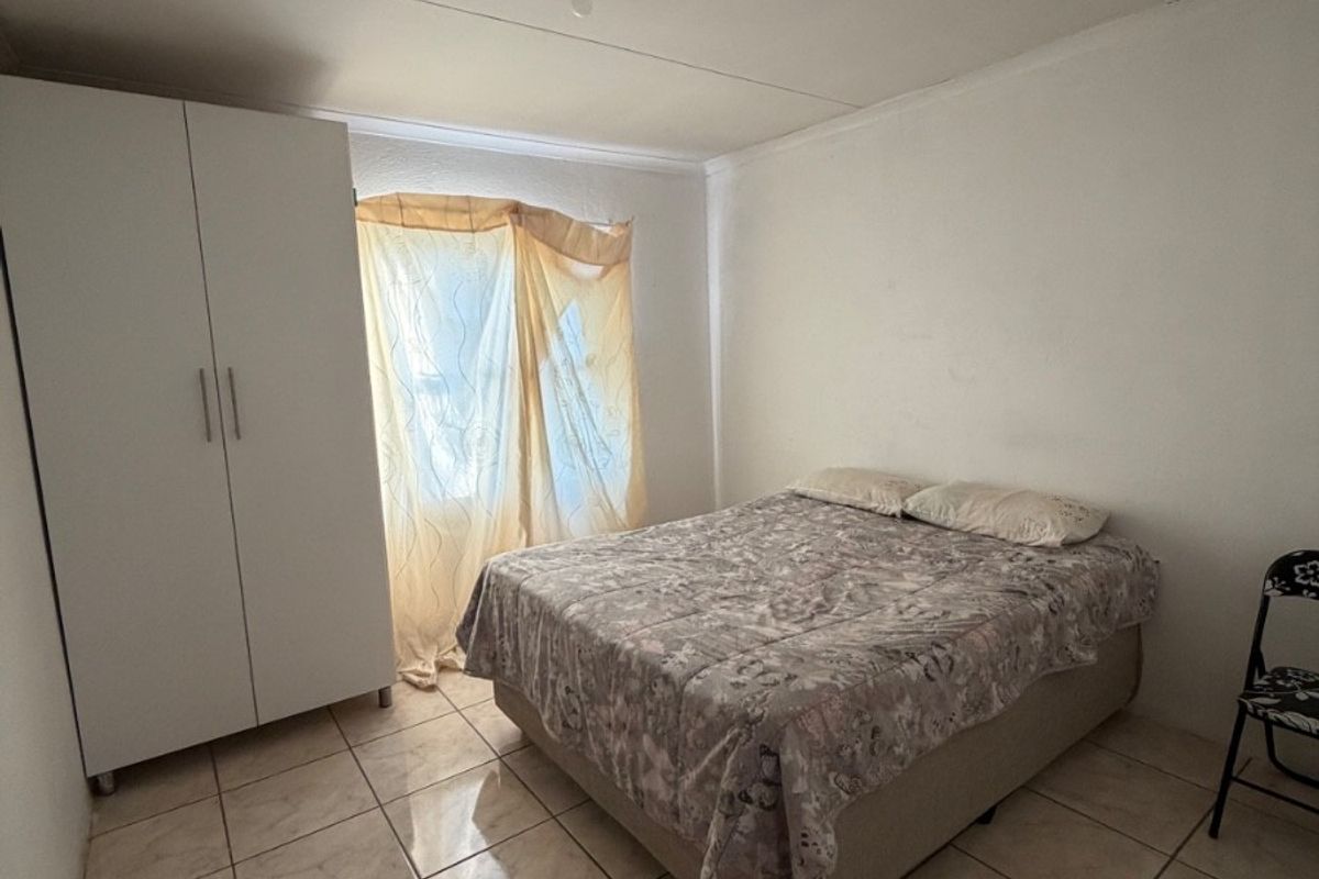 A functional bedroom featuring tiled flooring and a built-in wardrobe, offering a simple and practical living space.