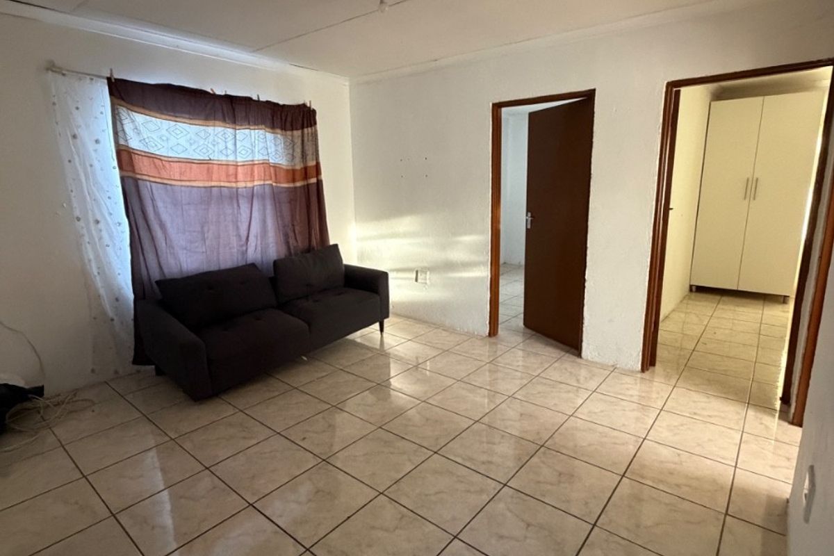 A simple living area featuring tiled flooring, neutral walls, and direct access to adjacent rooms, providing a functional and versatile space.