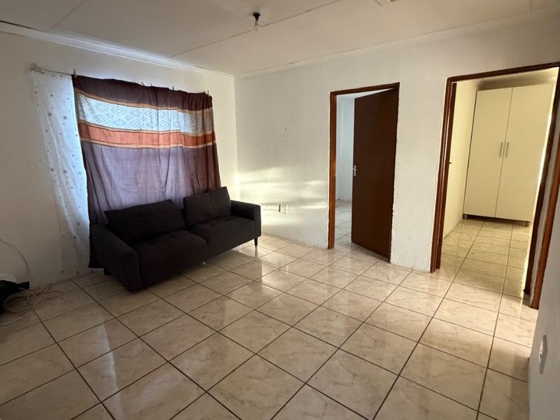 A simple living area featuring tiled flooring, neutral walls, and direct access to adjacent rooms, providing a functional and versatile space.