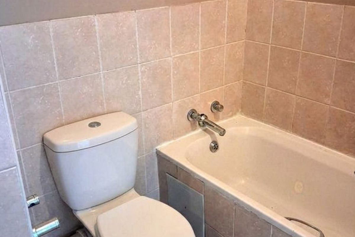 A functional bathroom featuring a standard bathtub with chrome fixtures and a close-coupled toilet, finished with neutral wall and floor tiling.