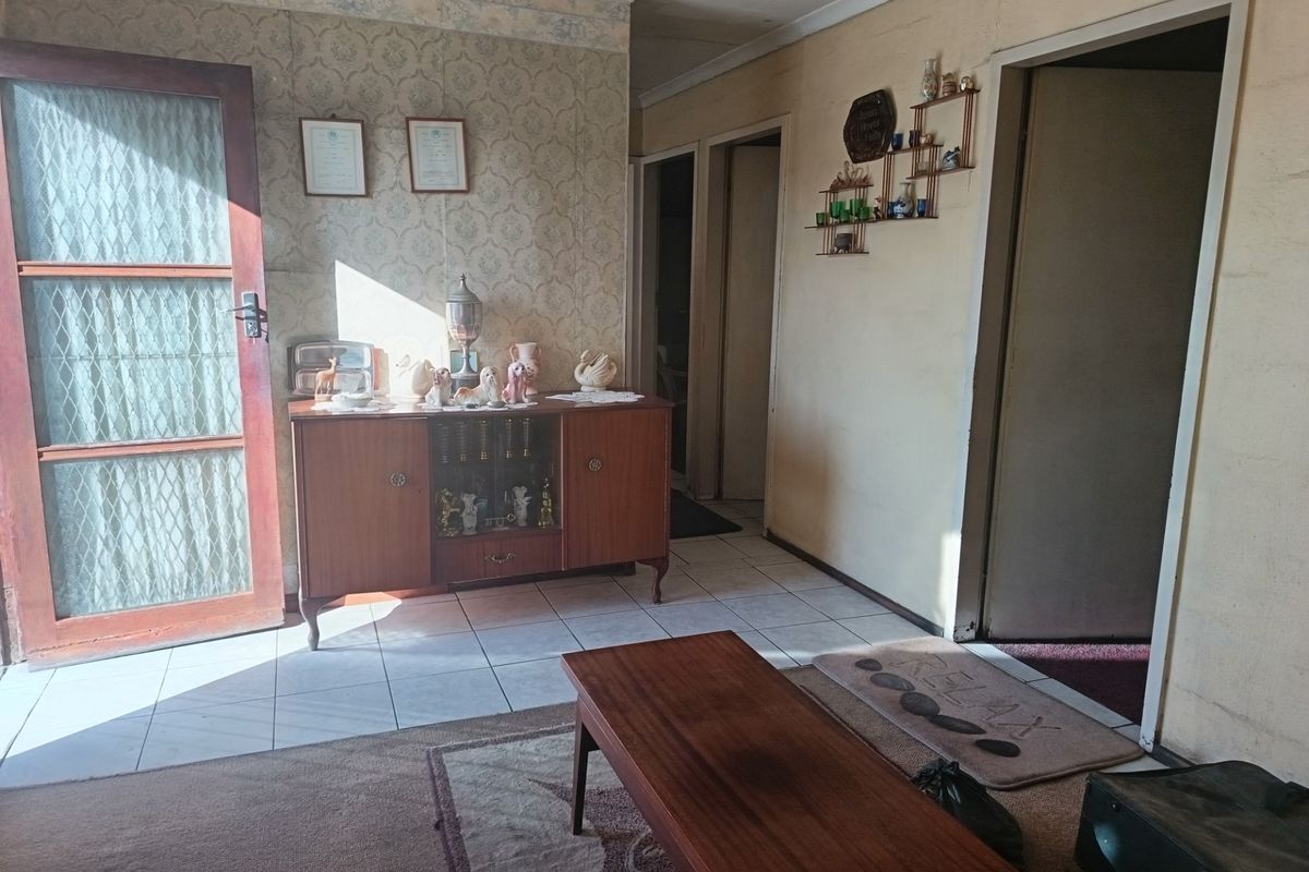 A dated living area featuring tiled flooring, patterned wallpaper, and multiple internal doorways leading to adjacent rooms.