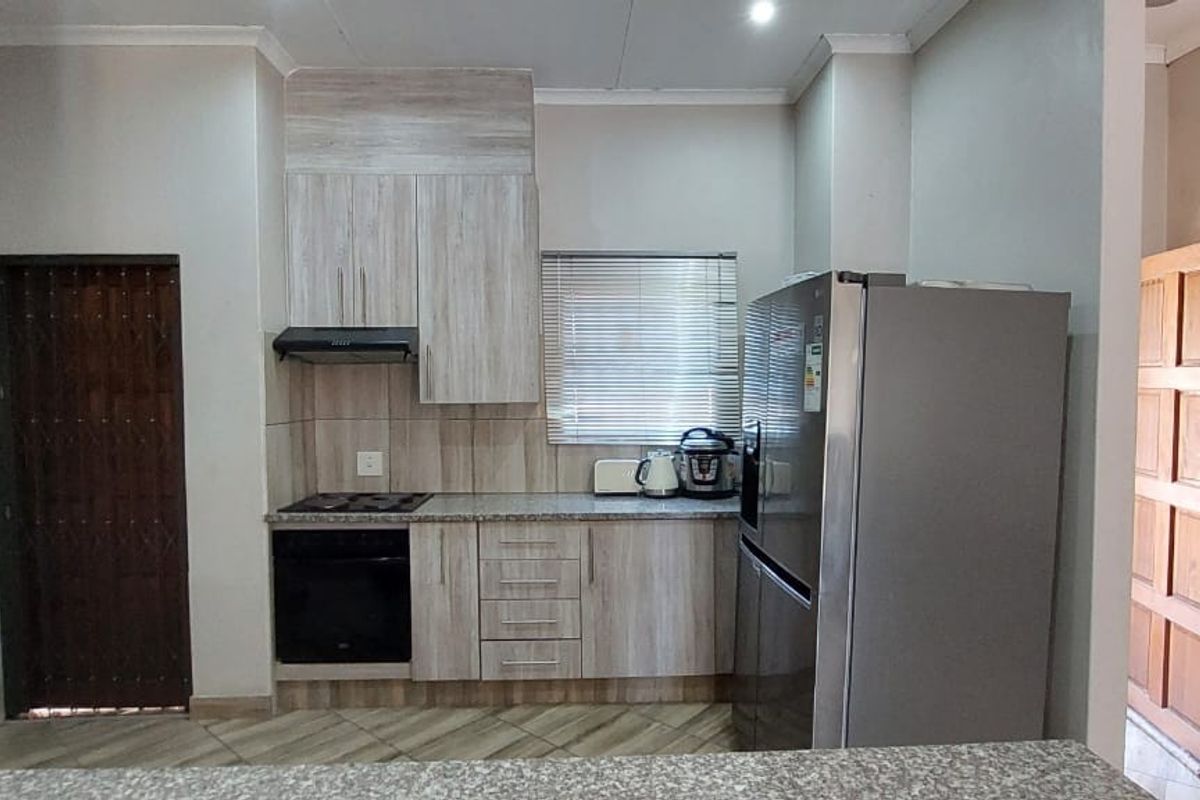 A functional kitchen featuring light wood-grain cabinetry, granite countertops, a built-in oven and hob, and an extractor fan.