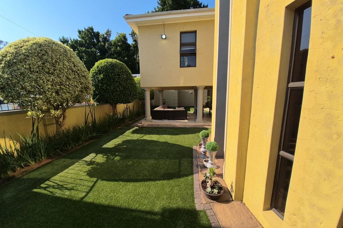 A well-maintained rear garden featuring artificial turf, landscaped borders, and a covered patio area supported by structural columns.