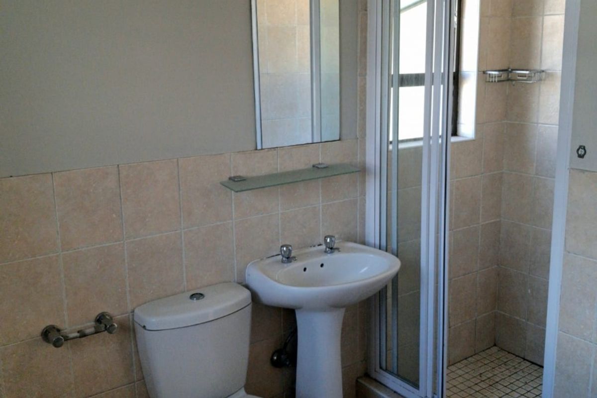 A functional bathroom featuring a pedestal basin, toilet, and a glass-enclosed shower with neutral wall and floor tiling.