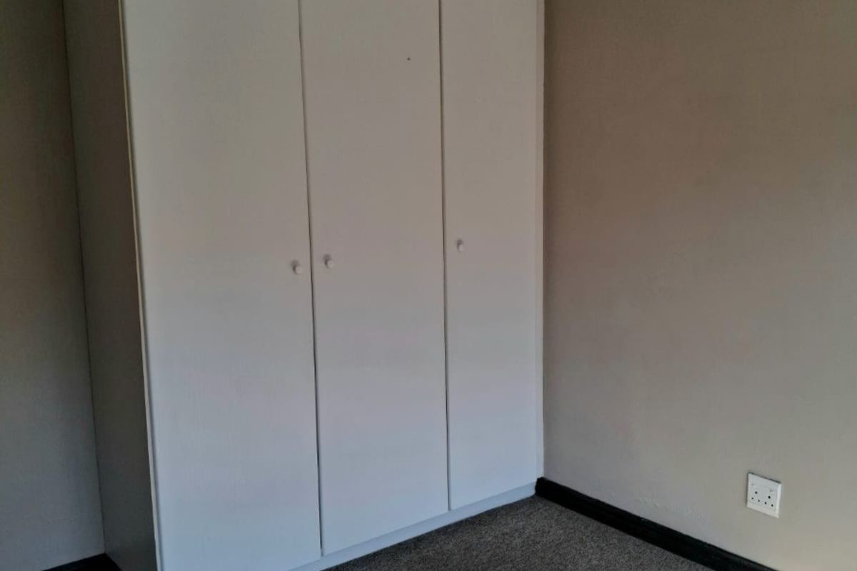 A clean, empty bedroom featuring neutral wall tones, carpeted flooring, and a functional built-in white wardrobe with ample storage space.