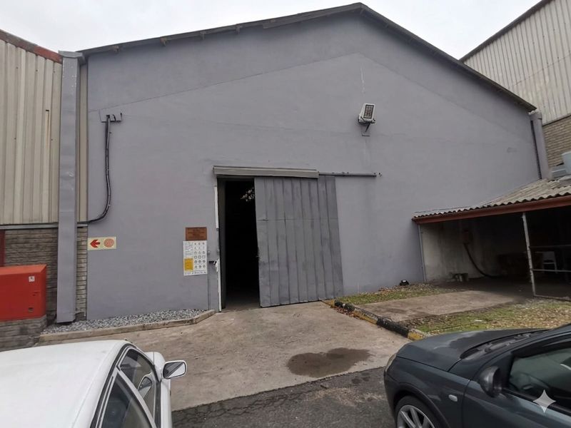 Industrial warehouse exterior featuring a large sliding metal door, concrete apron, and external security lighting.