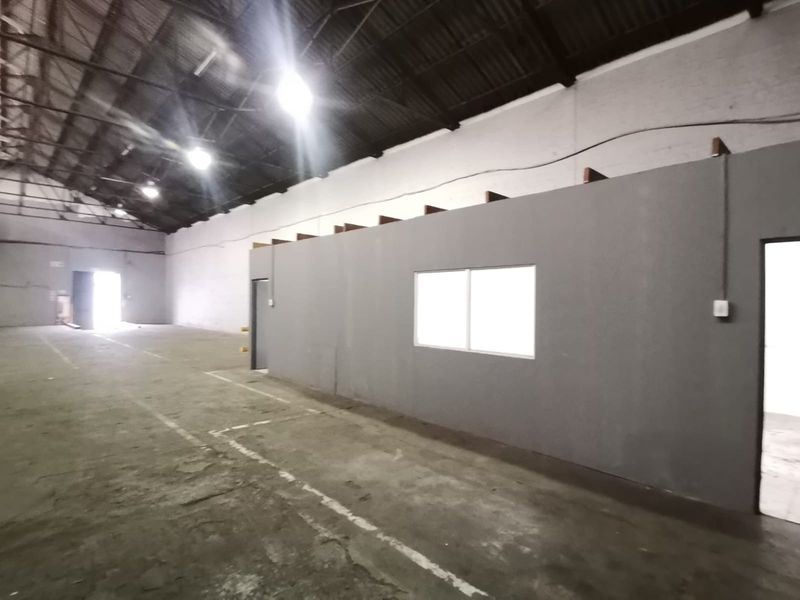 Spacious industrial warehouse interior featuring high vaulted ceilings, concrete flooring, and a partitioned office or utility area with integrated lighting.