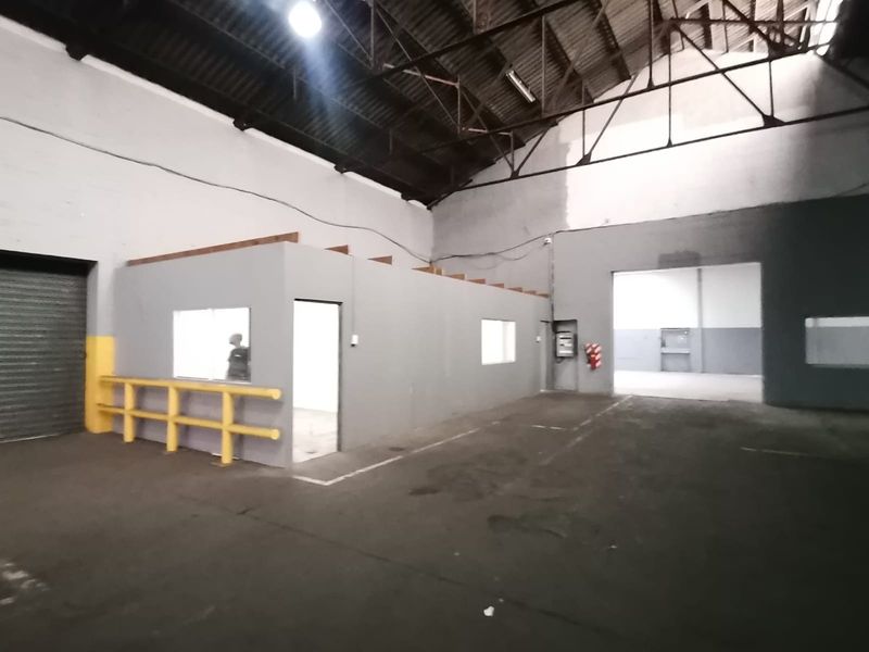 Spacious industrial warehouse featuring a high-truss roof, concrete flooring, and a partitioned office or utility room with safety railing.