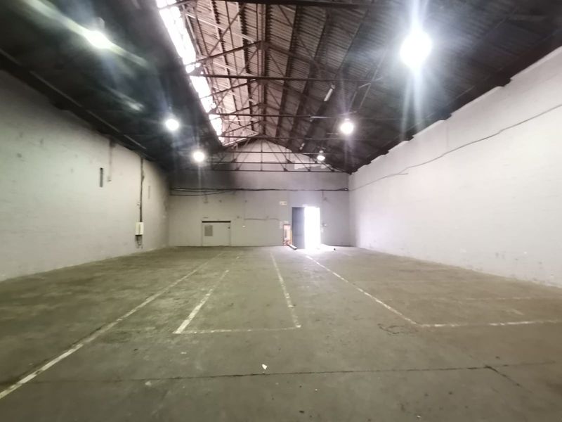 Spacious industrial warehouse featuring high vaulted ceilings, exposed steel trusses, concrete flooring, and ample natural light through roof panels.