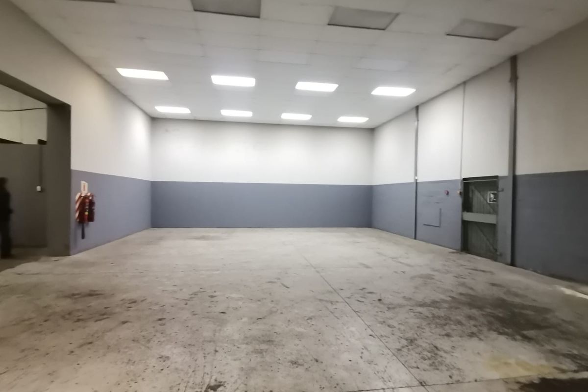 Spacious industrial warehouse unit featuring high ceilings with recessed lighting, concrete flooring, and a secure metal access door.