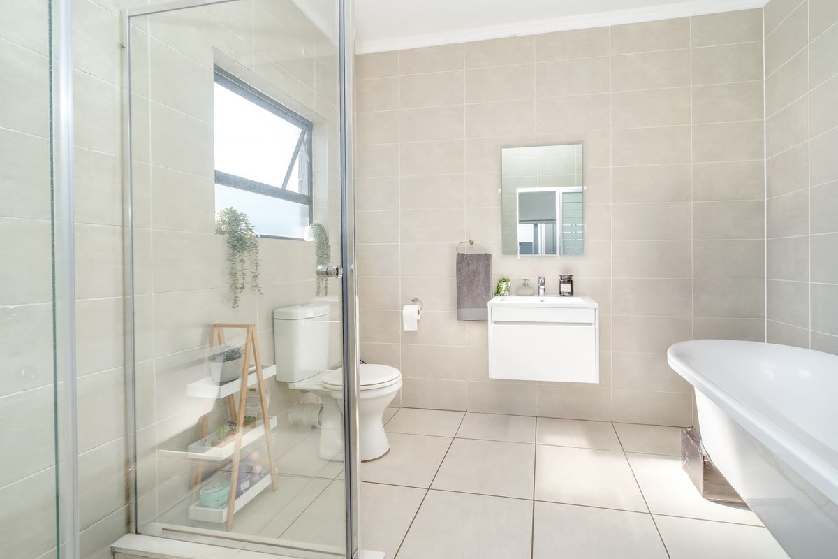 Modern bathroom featuring a glass-enclosed shower, a wall-mounted vanity, a freestanding bathtub, and neutral floor-to-ceiling tiling.