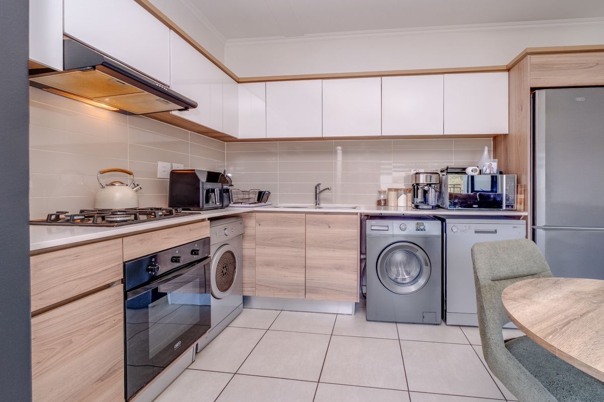 Modern kitchen featuring light wood-grain cabinetry, white upper cabinets, tiled backsplash, built-in oven, gas hob, and integrated laundry appliance connections.