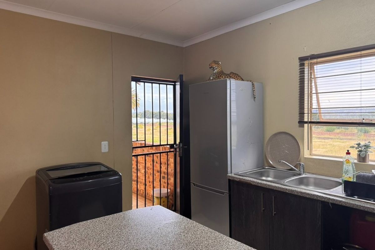 A functional kitchen area featuring laminate countertops, double sink, base cabinetry, and direct access to an outdoor space via a security gate.