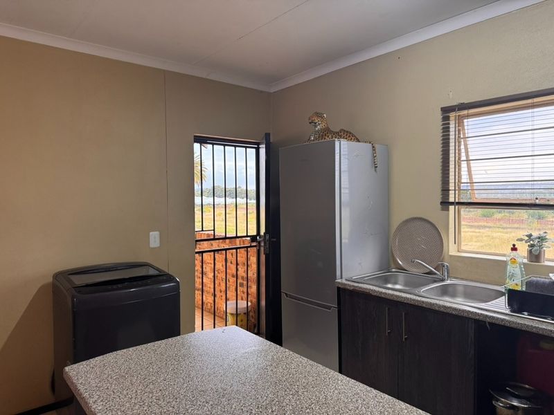 A functional kitchen area featuring laminate countertops, double sink, base cabinetry, and direct access to an outdoor space via a security gate.