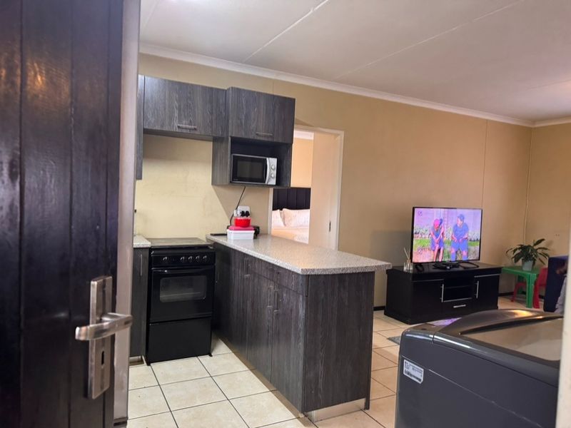 Open-plan living area featuring a compact kitchen with dark wood cabinetry, laminate countertops, and a freestanding oven, seamlessly flowing into the living space.