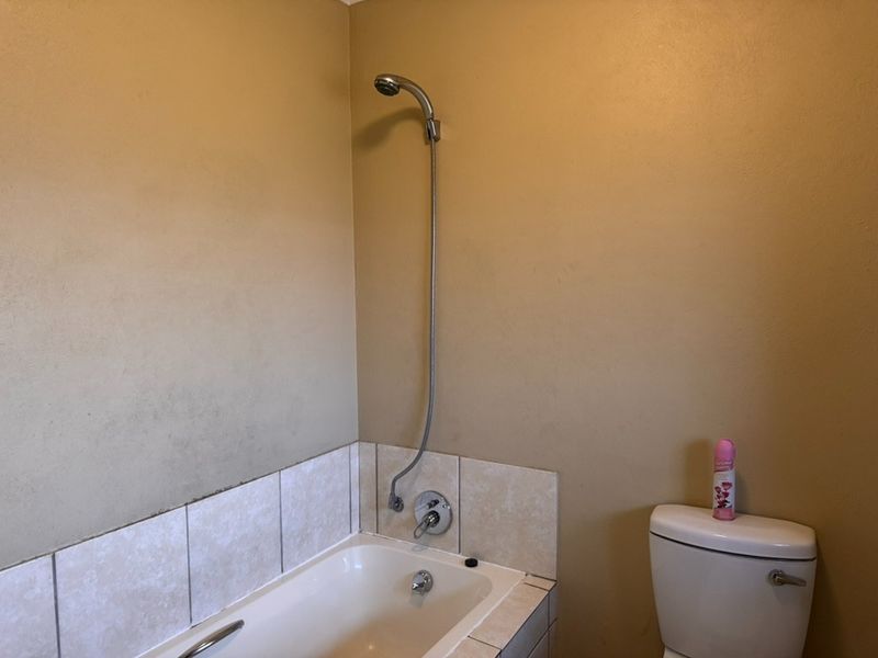 A functional bathroom featuring a bathtub with a shower attachment and a standard toilet, requiring cosmetic updates to the wall finishes and tiling.