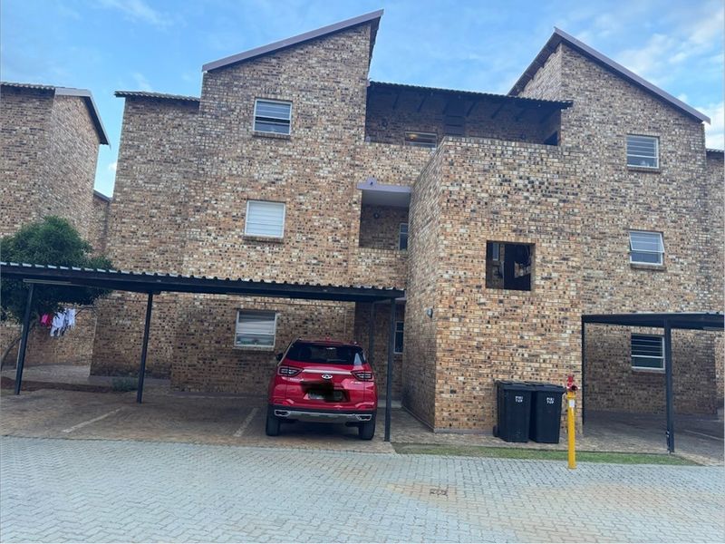 Exterior view of a multi-story face brick apartment complex featuring covered parking bays and paved driveway access.
