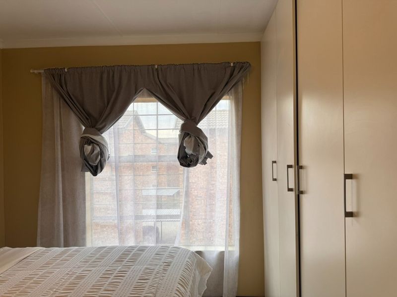 A bedroom featuring built-in cupboards and a window with security bars, offering a functional and practical living space.
