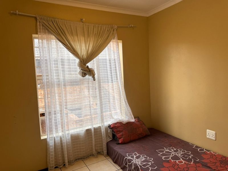 A compact bedroom featuring tiled flooring and a window fitted with security bars, offering a functional space ready for cosmetic updates.