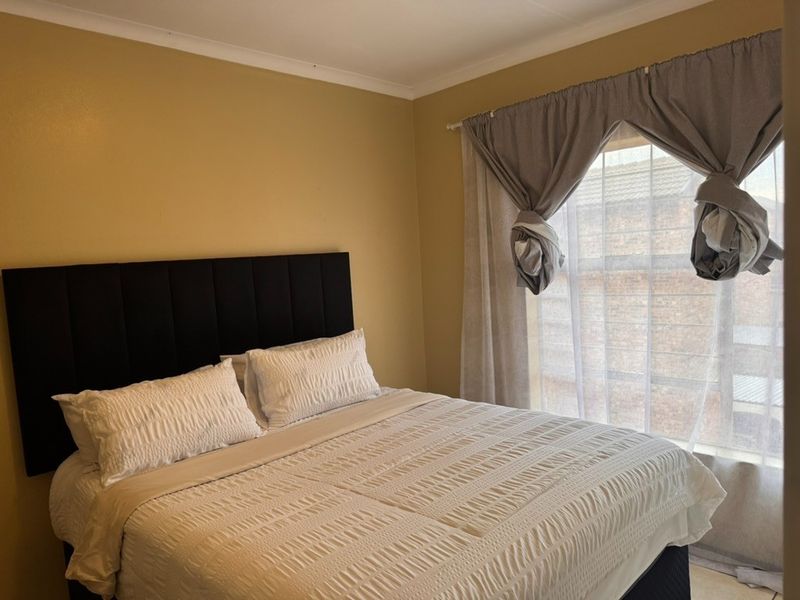 A standard bedroom featuring neutral wall paint and a window with fitted curtain tracks.