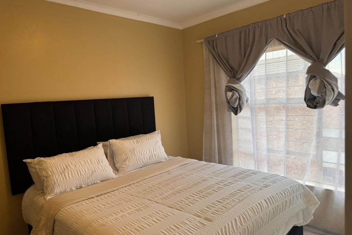 A standard bedroom featuring neutral wall paint and a window with fitted curtain tracks.