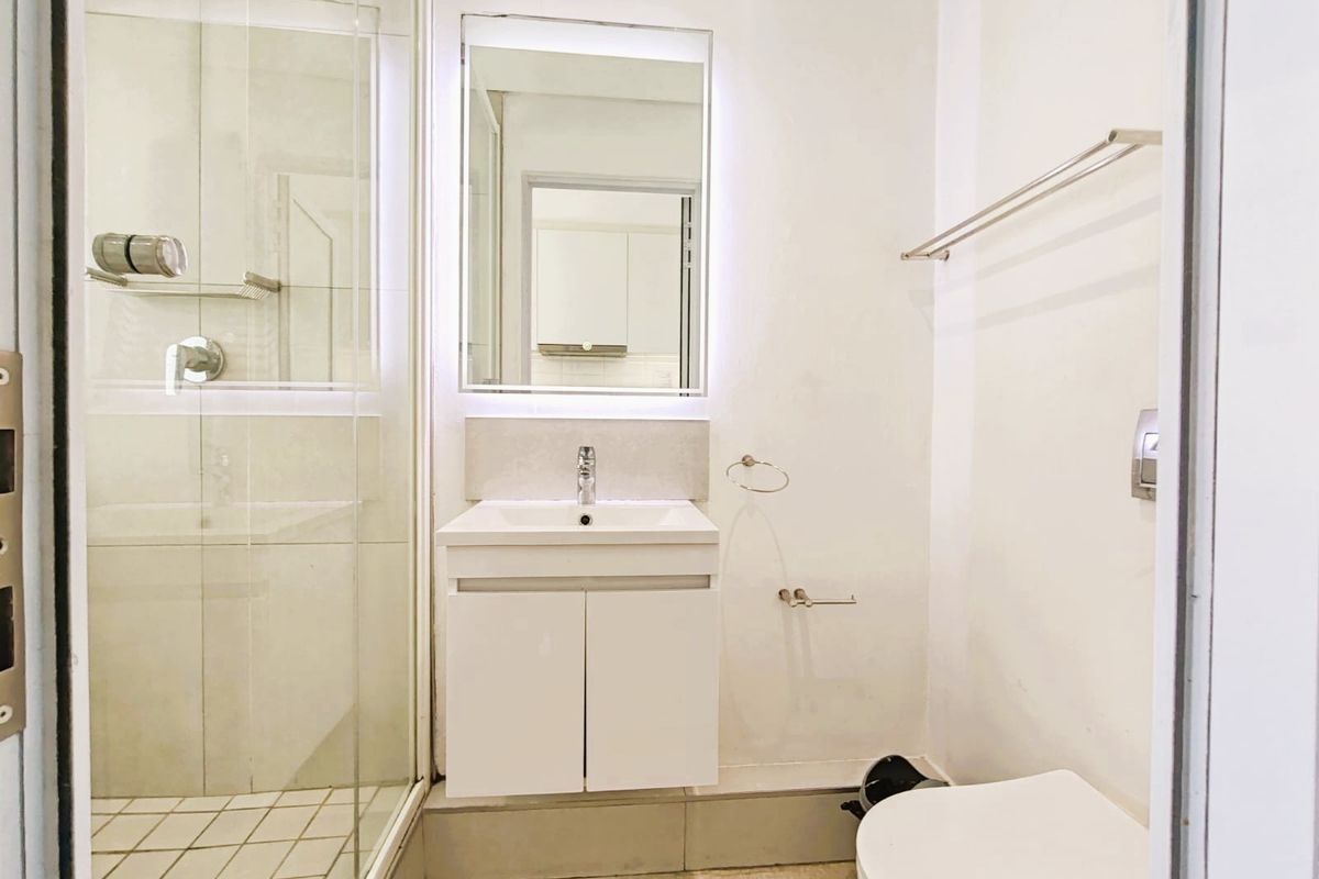 Modern bathroom featuring a glass-enclosed shower, vanity cabinet with integrated basin, and a wall-mounted mirror with LED lighting.