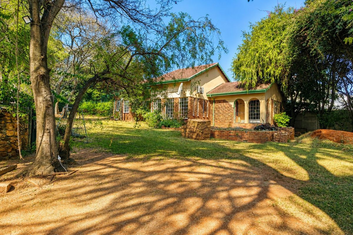 A view of the rear exterior of the house featuring brick facade, arched window details, and a spacious garden area with mature trees.