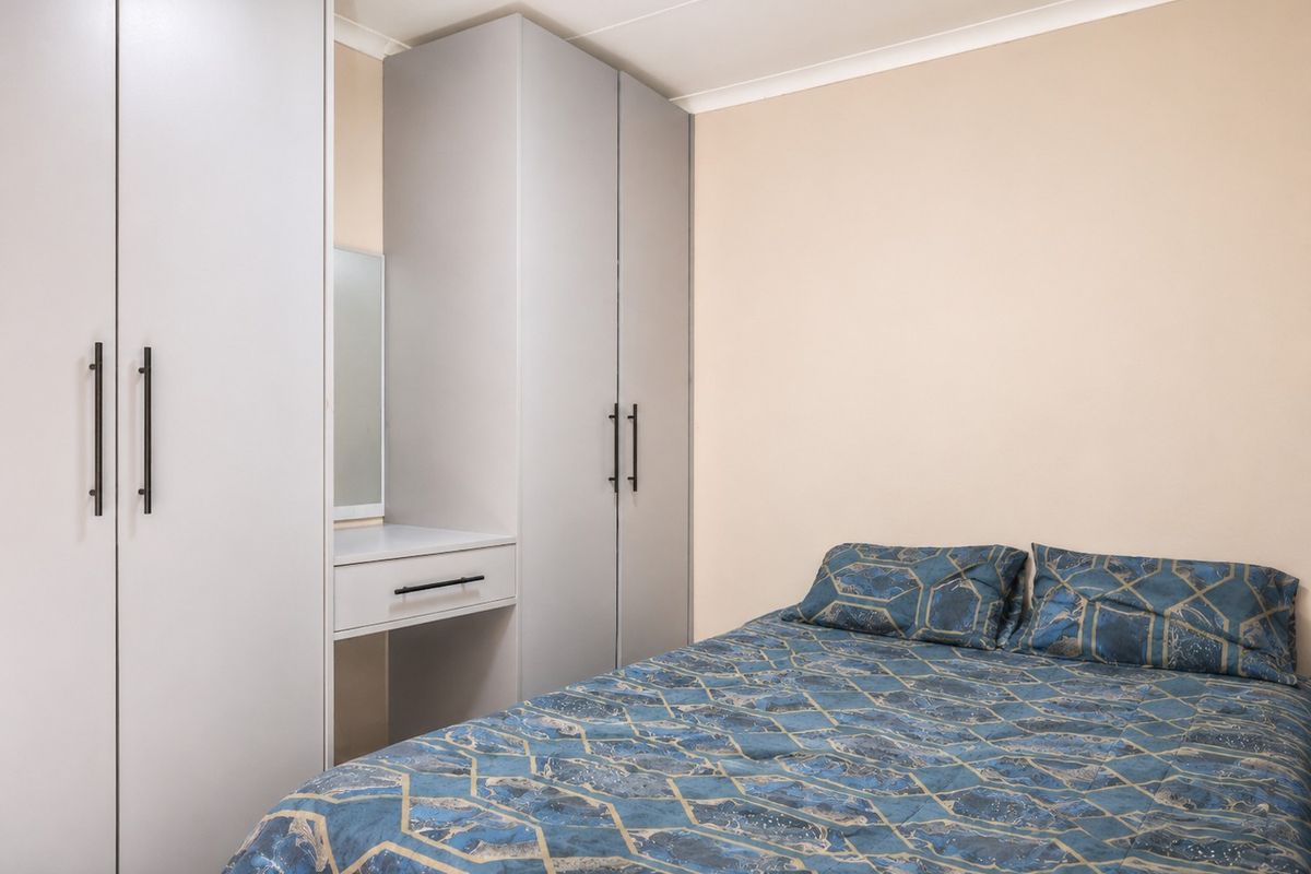 A well-maintained bedroom featuring built-in grey cabinetry with an integrated vanity unit and modern hardware.