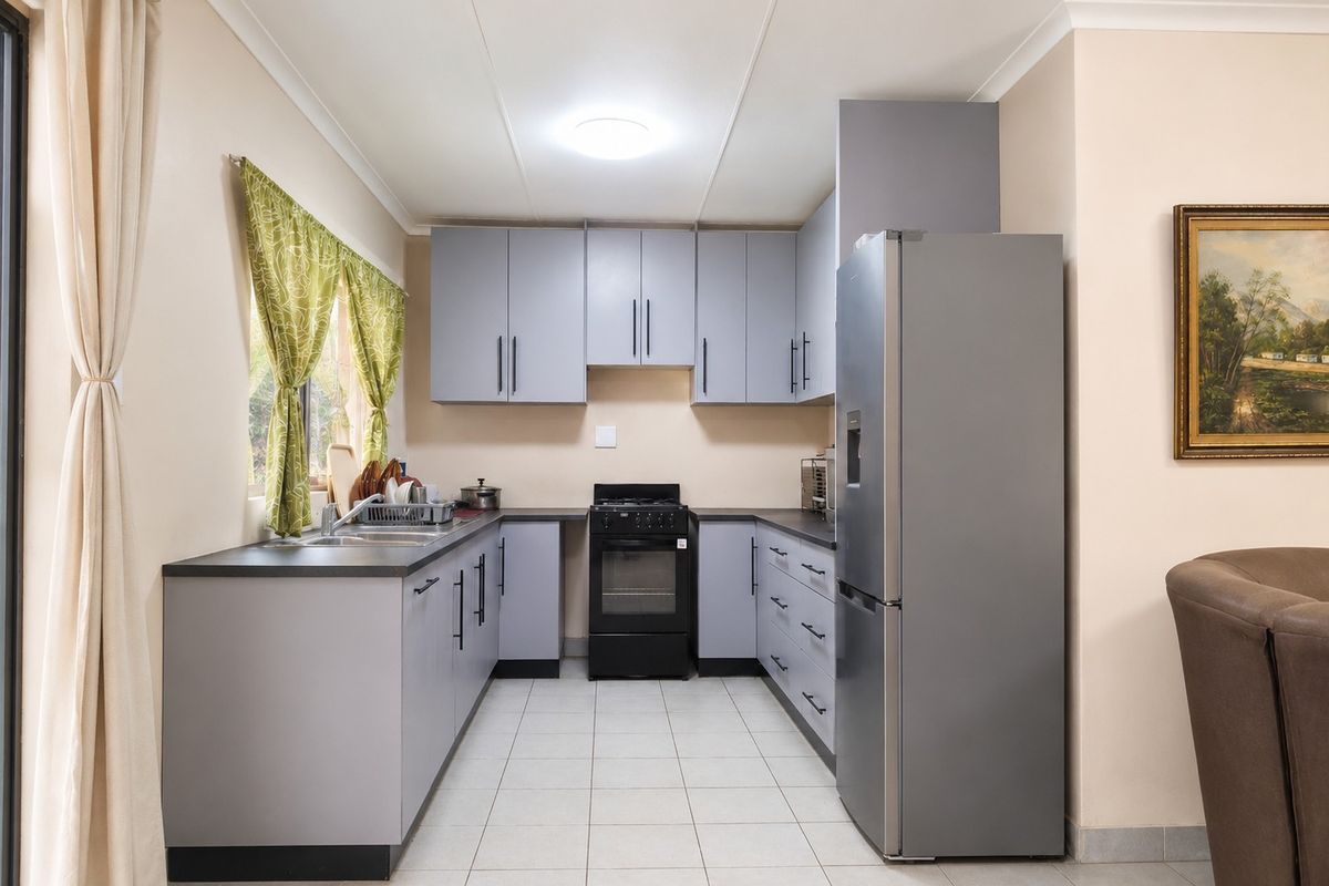 A functional kitchen featuring grey cabinetry, dark countertops, tiled flooring, and a built-in oven with extractor fan.