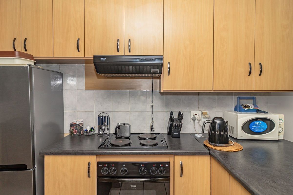 A functional kitchen featuring light wood cabinetry, dark laminate countertops, a built-in oven, electric hob, and an extractor fan.